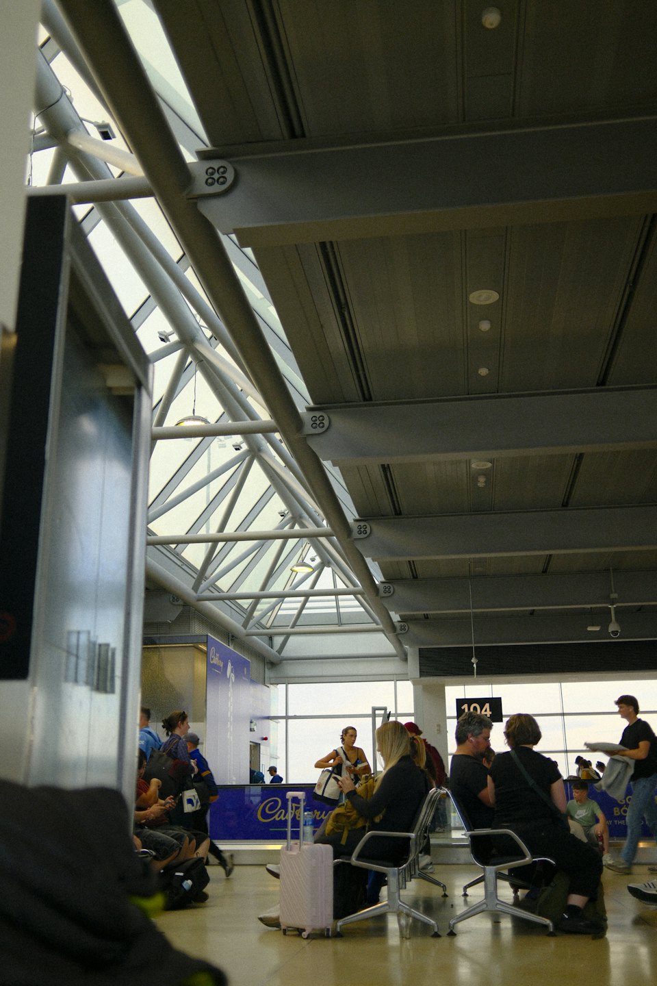 Reisende warten in einer modernen Flughafenlounge mit einer Glasbinderdecke.